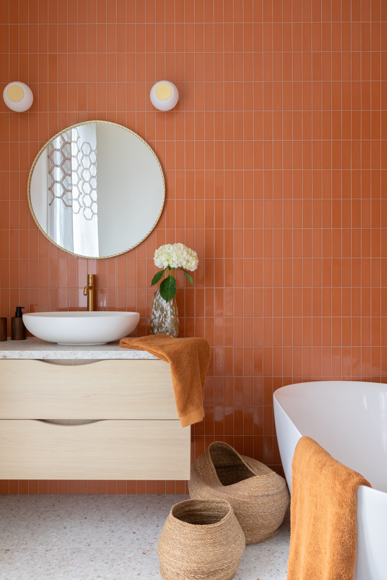 Salle de bain rénovée à Paris : faïence terracotta, meuble-vasque en bois suspendu sur plan terrazzo, miroir rond laiton et baignoire îlot